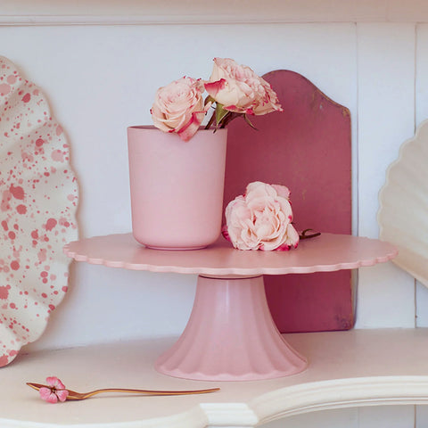 Pink cake stand with a vase and flowers on a white shelf