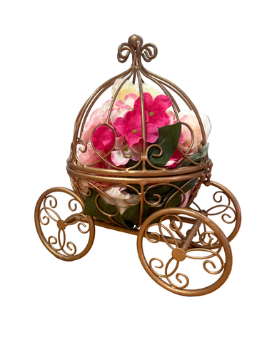 Decorative flower arrangement in a gold carriage-shaped container on a wooden surface with a gray background